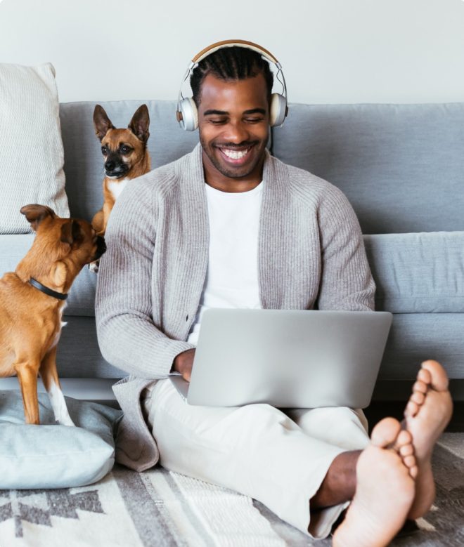 Man sitting on floor using laptop and headphones with two dogs in Virgina Home.
