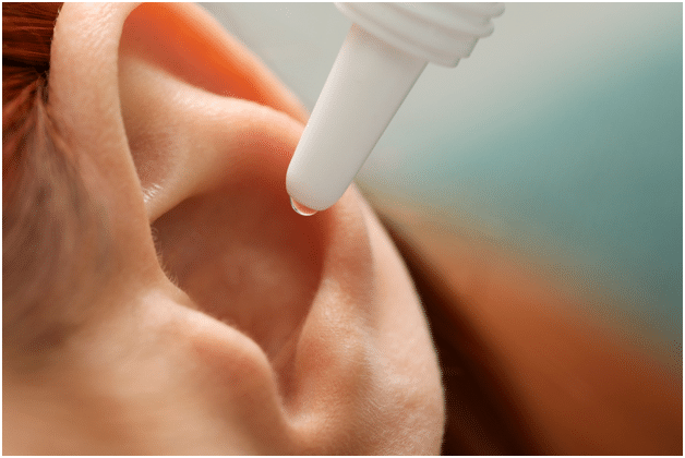 A woman applies ear drops to clean her ears and earwax.